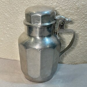 May include: A silver aluminum pitcher with a hinged lid and a handle. The pitcher has a faceted design and is made of metal.