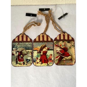 May include: Three vintage-style Christmas gift tags with images of Santa Claus. The tags are rectangular with red and white stripes and have a rustic look. The text on the tags reads "Merry Christmas" and "Christmas Greetings".