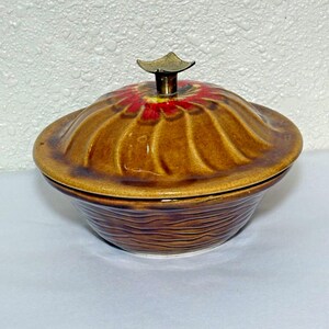 May include: A brown ceramic bowl with a lid. The lid has a swirl design and a small gold knob. The bowl has a wood grain design.