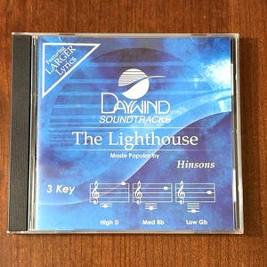 May include: A CD case with a blue and white cover. The text on the cover reads "DAYWIND SOUNDTRACKS The Lighthouse" and "Featuring LARGER Lyrics." Below the title are musical notes and the text "3 Key, High D, Med Bb, Low Gb."