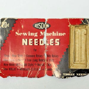 Puede incluir: Embalaje vintage de agujas de máquina de coser. El embalaje de cartón rojo y negro presenta la marca "RISDON" y el texto "Sewing Machine NEEDLES". El paquete incluye un recipiente de plástico transparente que contiene agujas. El texto "Made in U.S.A." es visible.