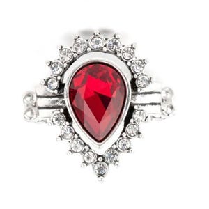 Op de afbeelding: Een zilveren ring met een grote rode druppelvormige edelsteen omringd door kleinere witte edelstenen.