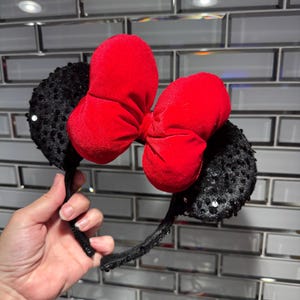 May include: Black headband with a large red velvet bow and black sequined ears.