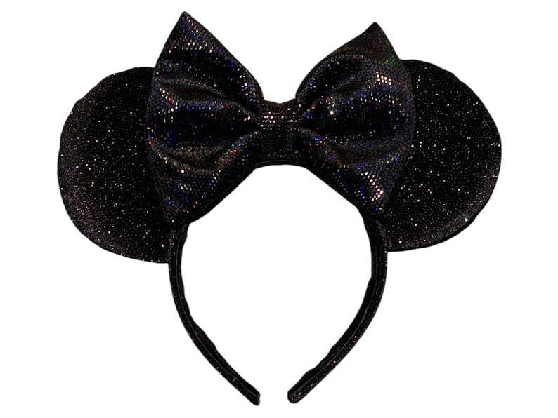 May include: A black headband featuring two circular ears and a large central bow. The entire surface of the headband, ears, and bow is covered in a fine, dark, shimmering glitter material that reflects light with subtle iridescent highlights.