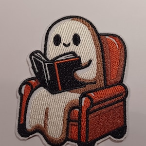 May include: Embroidered patch of a white ghost reading a book while sitting in a brown and orange armchair.