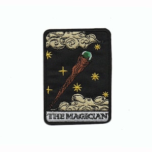 May include: Black rectangular patch with a tarot card design. It shows a brown staff with a green orb, surrounded by gold stars and clouds. The text "THE MAGICIAN" is at the bottom of the patch.