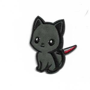 May include: An embroidered patch of a cartoon cat in grey, with a red and white knife sticking out of its back.
