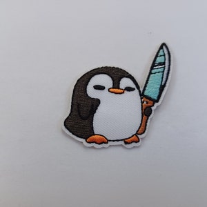 May include: Embroidered patch of a cartoon penguin holding a knife. The penguin is black and white with orange feet. The knife is blue and white.
