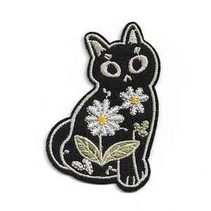 May include: Embroidered black cat patch featuring white daisy flowers with yellow centres and green leaves. The cat has a white outline. The patch is set against a white background.