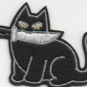 Peut inclure: Patch brodé noir représentant un chat avec un couteau autour du cou. Le chat a des yeux blancs et un contour argenté.