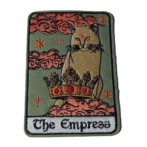 May include: An embroidered patch depicting a white cat wearing a gold crown, sitting on pink clouds against a green background. The text "The Empress" is written below the cat.