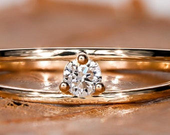 May include: A delicate gold ring with a single round diamond set in the center. The ring features a double band design, with one band slightly raised above the other.