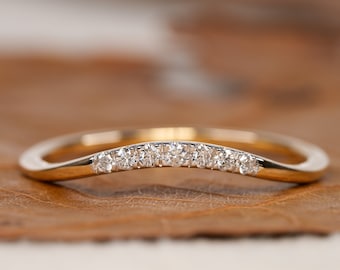 May include: A delicate gold band with a curved shape and a row of small diamonds set in the center.