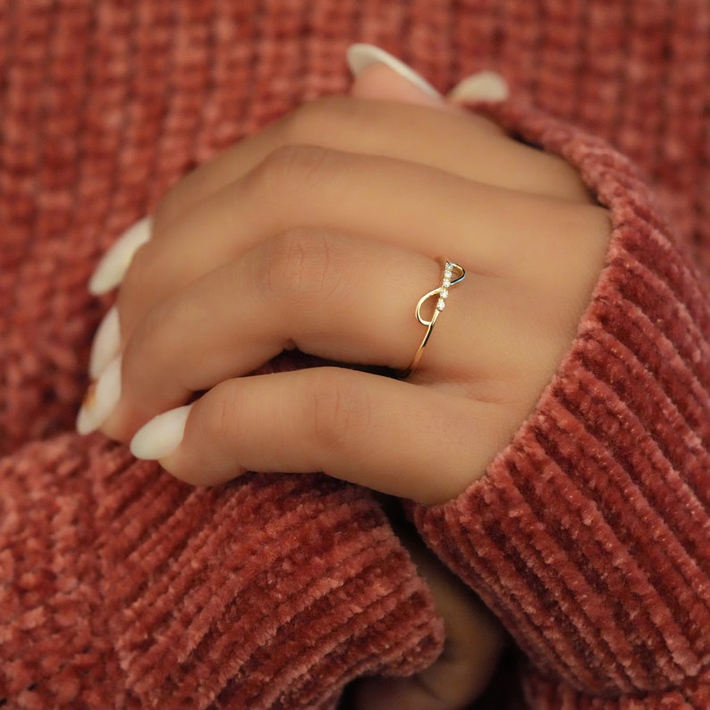 K&ouml;nnte beinhalten: Ein goldener Unendlichkeitsring mit kleinen, klaren Steinen, die in die Band eingefasst sind.