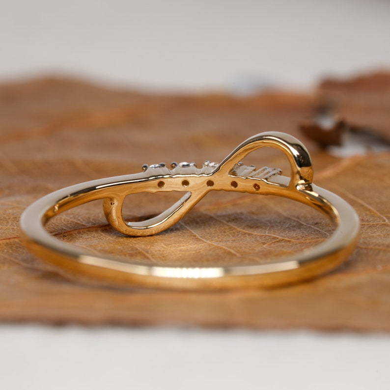 K&ouml;nnte beinhalten: Ein goldener Unendlichkeitsring mit kleinen, klaren Steinen, die in die Band eingefasst sind.