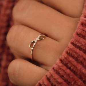 K&ouml;nnte beinhalten: Ein goldener Unendlichkeitsring mit kleinen Diamanten, die in die Band eingefasst sind.