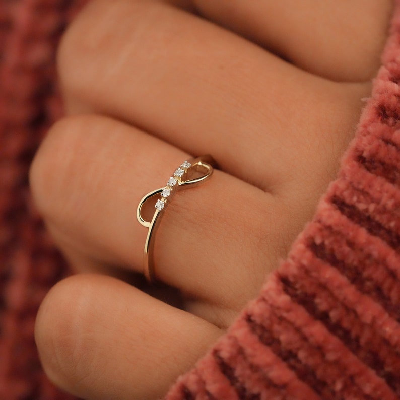 K&ouml;nnte beinhalten: Ein goldener Unendlichkeitsring mit kleinen Diamanten, die in die Band eingefasst sind.