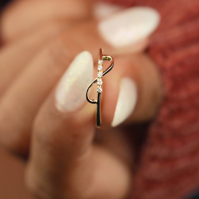 K&ouml;nnte beinhalten: Ein goldener Ring mit einem zarten Unendlichkeitsdesign und kleinen klaren Steinen.