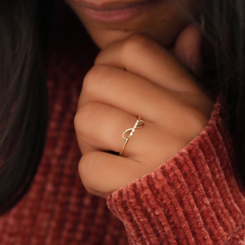 K&ouml;nnte beinhalten: Ein goldener Unendlichkeitsring mit kleinen Diamanten, die in die Band eingefasst sind.
