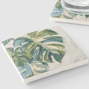 May include: Two square coasters with a white background and a green and blue tropical leaf design. The coasters are made of ceramic and are perfect for protecting surfaces from spills.