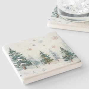 May include: Set of two square ceramic coasters with a winter forest scene. The coasters feature a snowy landscape with pine trees and snowflakes.