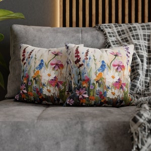 Op de afbeelding: Twee decoratieve kussens met een bloemenprint met een verscheidenheid aan kleurrijke bloemen, waaronder roze, paarse, blauwe en gele bloemen op een witte achtergrond.