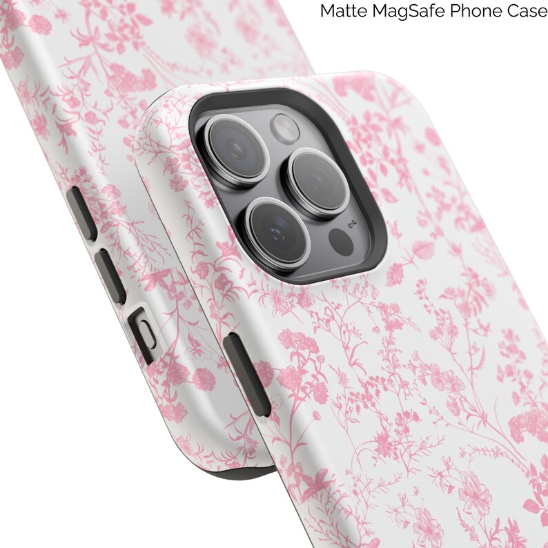 Pode incluir: Uma capa de telefone branca com um padr&atilde;o floral rosa. A capa tem uma sali&ecirc;ncia de c&acirc;mera elevada e um acabamento fosco. O texto "Matte MagSafe Phone Case" &eacute; vis&iacute;vel no canto superior direito da imagem.