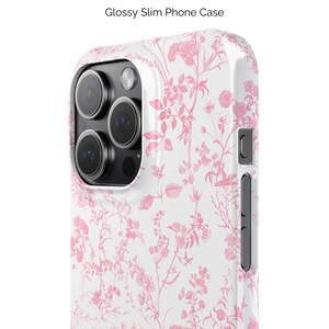 Pode incluir: Uma capa de telefone branca com um padr&atilde;o floral rosa. A capa tem um acabamento brilhante e um recorte para a lente da c&acirc;mera.