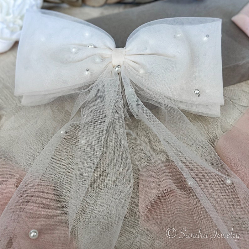 Ivory Bow Veil with Pearls. Drape yourself in opulence with the pearl-strewn layers of the 2024 Trendy Bow Veil, available in two sizes for personalized elegance – an exquisite addition to your bridal ensemble.