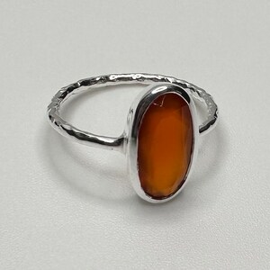 Peut inclure: Une bague en argent avec une bande martel&eacute;e et une pierre de cornaline de forme ovale.