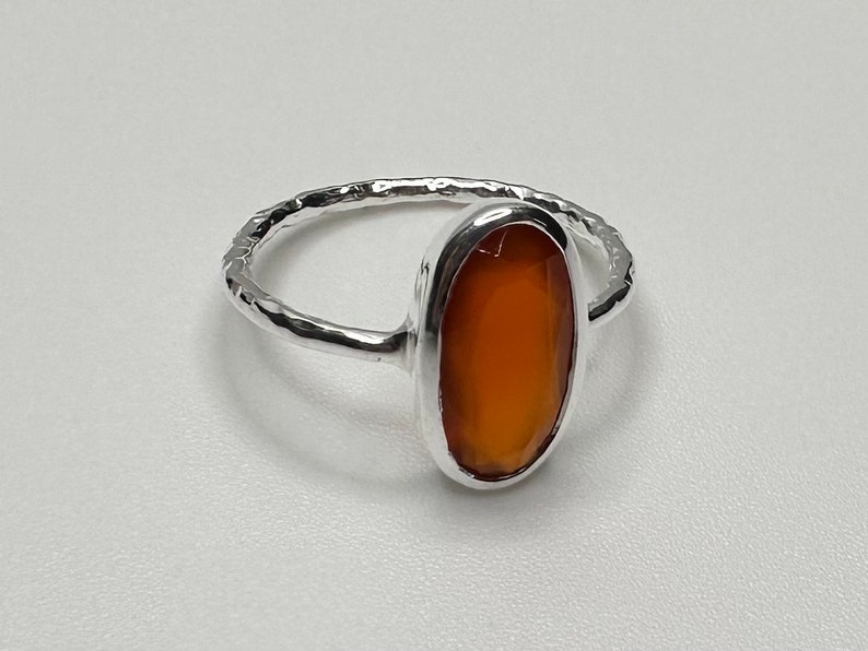Peut inclure: Une bague en argent avec une bande martel&eacute;e et une pierre de cornaline de forme ovale.