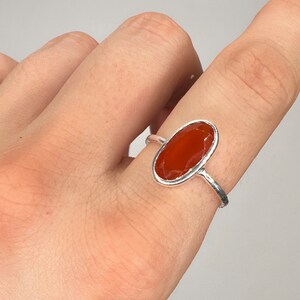 Peut inclure: Une bague en argent avec une pierre de cornaline de forme ovale. La bague est port&eacute;e sur un doigt.