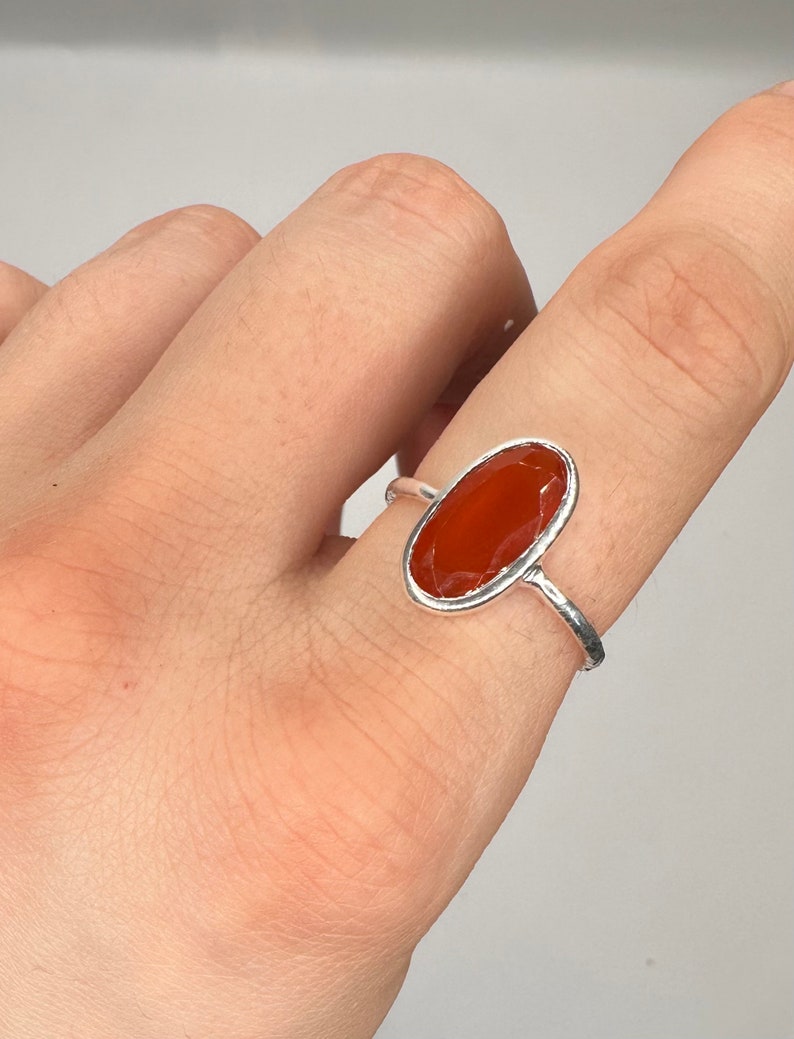 Peut inclure: Une bague en argent avec une pierre de cornaline de forme ovale. La bague est port&eacute;e sur un doigt.