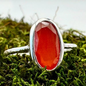 Peut inclure: Une bague en argent avec une grande pierre de cornaline de forme ovale. La pierre est de couleur rouge fonc&eacute; et a une finition lisse et polie.