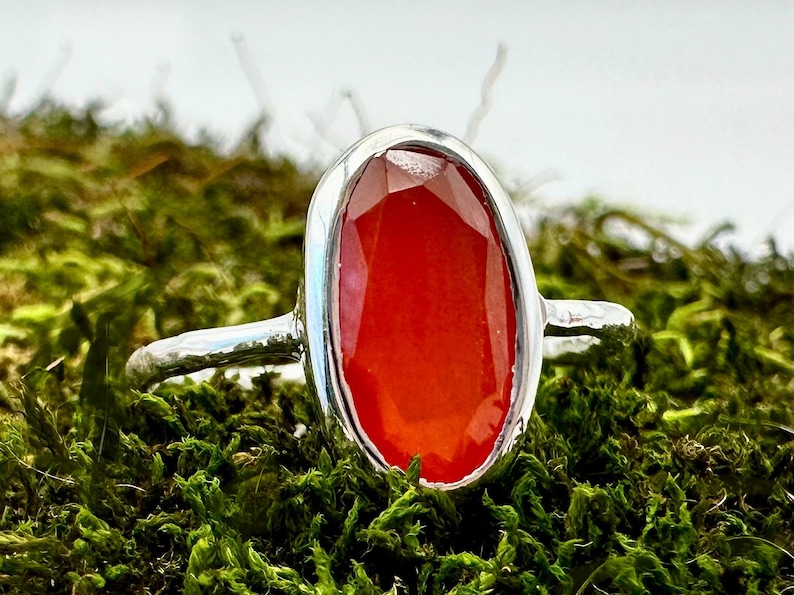 Peut inclure: Une bague en argent avec une grande pierre de cornaline de forme ovale. La pierre est de couleur rouge fonc&eacute; et a une finition lisse et polie.