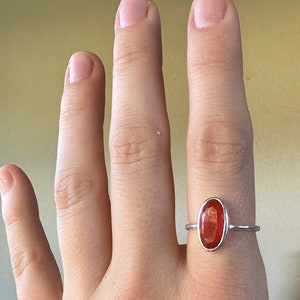 Peut inclure: Une bague en argent avec une pierre ovale rouge. La bague est sur le doigt d'une personne.