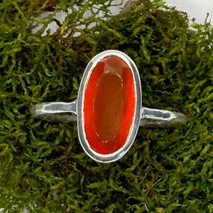 Peut inclure: Une bague en argent avec une pierre de cornaline de forme ovale. La cornaline est de couleur orange fonc&eacute; et est sertie dans une b&eacute;li&egrave;re en argent.