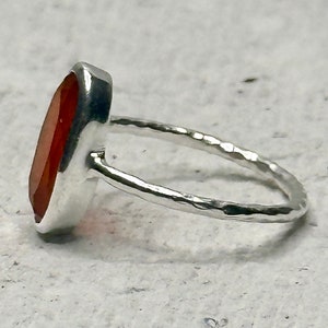 Peut inclure: Une bague en argent avec une grande pierre pr&eacute;cieuse orange de forme ovale. La bande de la bague est martel&eacute;e et a une finition textur&eacute;e.
