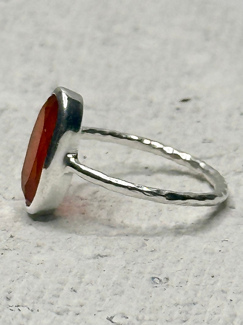 Peut inclure: Une bague en argent avec une grande pierre pr&eacute;cieuse orange de forme ovale. La bande de la bague est martel&eacute;e et a une finition textur&eacute;e.