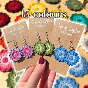May include: Three pairs of crocheted flower earrings on brown cards with the text "Cup of Coffee Crochet" on each card. The earrings are in shades of purple, green, and blue. The text "15 colours" is displayed above the cards.