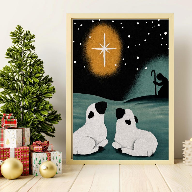 May include: A framed art print featuring a night scene with two white lambs with black ears and faces resting on a dark teal ground. Above them, a bright white star glows in a golden halo against a black sky filled with white dots.