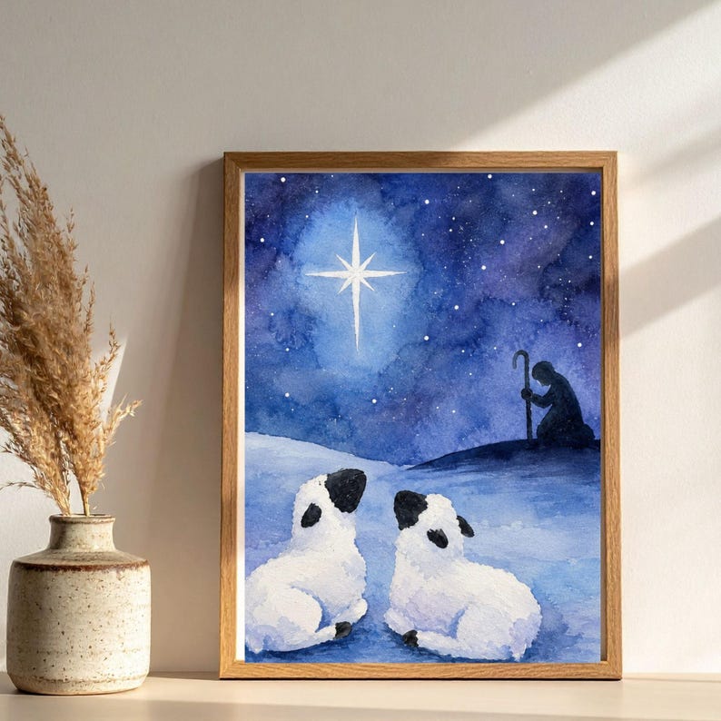 May include: A framed watercolor print featuring a dark blue night sky with a bright white star, a silhouette of a shepherd holding a staff on a hill, and two white sheep with black ears and faces resting in the foreground on a snowy landscape.