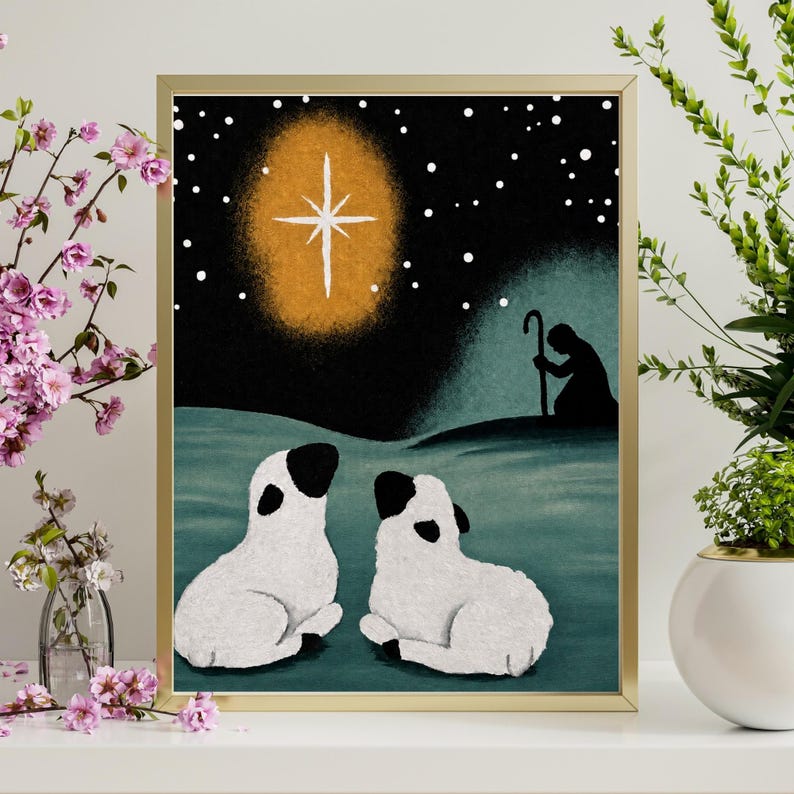 May include: A framed art print featuring a dark night sky with a bright glowing star, a silhouette of a shepherd with a staff, and two white lambs with black ears and faces resting on a teal ground. The scene depicts a starry night landscape.