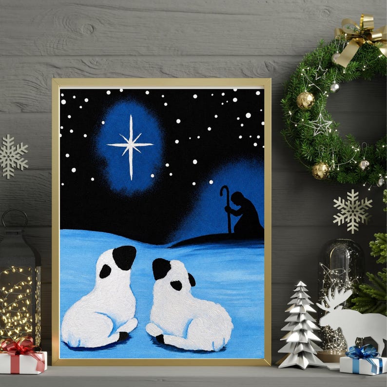 May include: A framed painting depicting a night scene with two white sheep with black ears and faces resting on a blue snowy ground. Above them, a bright white star shines in a dark blue sky, while a silhouette of a shepherd with a staff stands nearby.