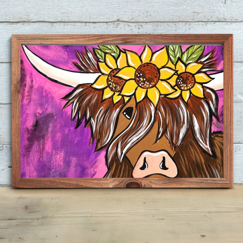 May include: A painting of a Highland cow with a crown of sunflowers on its head. The cow is brown and white with a pink nose. The background is a vibrant purple.
