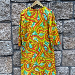 May include: A vintage 1960s dress with a psychedelic print in shades of green, red, blue, and white. The dress has a round neckline and long sleeves.
