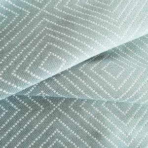 以下が含まれることがあります： 薄い青色の生地のクローズアップ。白いひし形の模様が施されています。生地は質感があり、わずかに光沢があります。