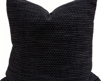 May include: A square decorative pillow with a textured, geometric pattern. The pillow features a dark gray and black color scheme, with a repeating triangle design across the surface. The pillow is designed for home decor.