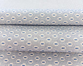 May include: A folded piece of white fabric featuring a repeating geometric pattern of small blue rectangles and dots. The textile has a textured weave with horizontal lines of blue dashes interspersed with solid blue squares across the surface.