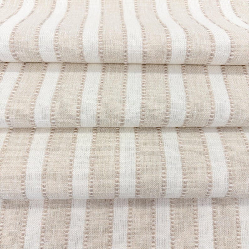 May include: A folded textile fabric featuring a repeating pattern of vertical stripes in alternating shades of beige and white. The beige stripes are textured with a subtle, raised dot pattern, while the white stripes appear smooth.